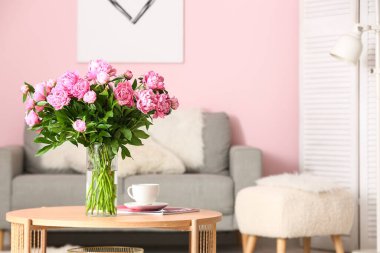 Kahve masasında pembe şakayık vazosu ve oturma odasında kanepe.