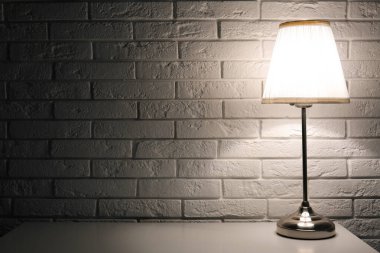 Beyaz tuğla duvarın yanındaki masada parlayan lamba.