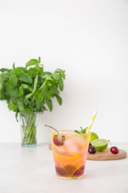 Bir bardak lezzetli vişneli limonata, nane ve beyaz arka planda limonlu ahşap tahta.