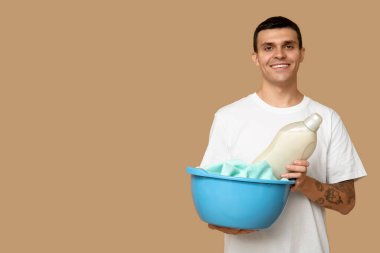 Havlu içinde kirli havlular ve bej arka planda bir şişe deterjan olan genç bir adam.