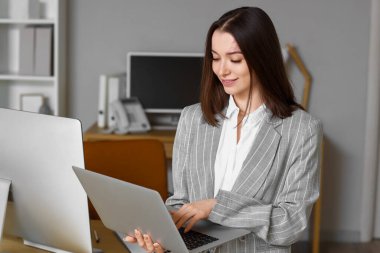 Genç iş kadını ofiste dizüstü bilgisayarla çalışıyor.