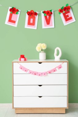 Çekmecelerin üzerinde hediye kutuları ve yeşil duvarın yanında aşk sözcüğü var. Sevgililer Günü kutlaması