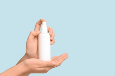 Mavi arka planda bir şişe kozmetik spreyi olan kadın elleri.