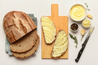 Tahta tahta ekmek dilimleri, taze tereyağı ve beyaz arka planda farklı baharatlar.