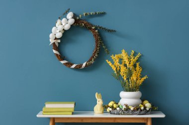 Tavşanlı masa, mimoza çiçekleri vazosu ve duvarda geleneksel Paskalya çelengi.