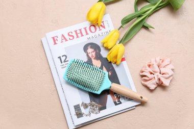 Saç fırçası, ipek toka ve bej arka planda lale çiçekleri olan dergiler.