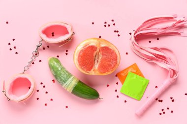 Seks oyuncaklı prezervatifler, pembe arka planda taze greyfurt ve salatalık. Seks eğitimi