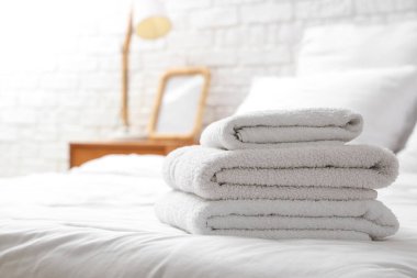 Evdeki beyaz yatağa yığılmış yumuşak havlular, yakın çekim.