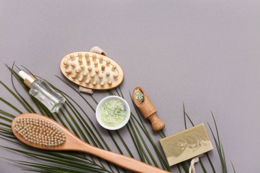 Masaj vücut fırçaları, deniz tuzu, palmiye yaprağı, sabun çubuğu ve gri arkaplanda doğal kozmetik ürünler içeren kompozisyon