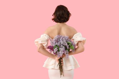 Pembe arka planda çiçek açan bir buket leylak çiçekli genç kadın.