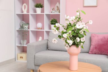 Rahat kanepesi, sehpası ve çiçek açan ağaç dalları olan şık bir oturma odası.