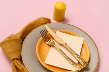 Altın çatal bıçak takımı ve pembe arka planda mum olan güzel bir masa.