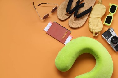 Seyahat yastığı, bilet, pasaport ve turuncu arka planda plaj aksesuarları.