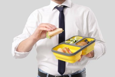 Elinde beslenme çantası ve gri arka planda lezzetli bir sandviç tutan genç adam.