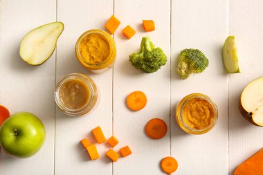 Sağlıklı bebek mamaları üzerine cam kavanozlar ve hafif ahşap arka plandaki malzemeler.