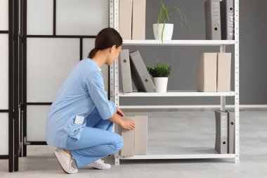 Genç kadın resepsiyonist hastanedeki raflardan klasör alıyor.