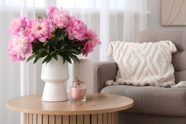 Sehpanın üzerinde pembe şakayık çiçekleri olan vazo şık oturma odasında yumuşak koltuğun yanında, yakın plan.