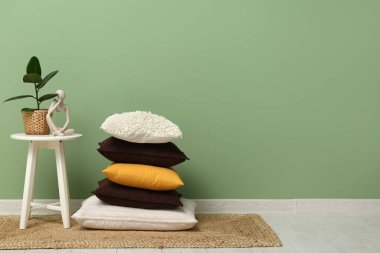 Halıdaki yastık yığını ve yeşil duvarın yanındaki sehpanın üzerinde insan figürü olan bitki.