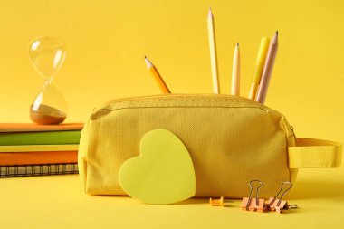Sarı zemin üzerinde farklı kırtasiye malzemesi olan kalem kutusu