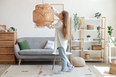 Genç bir kadın evdeki lambaya ampul takıyor.