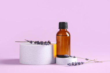 Eflatun arkaplanda bir şişe kozmetik yağı ve lavanta çiçekleri bulunan dekoratif podyumlar