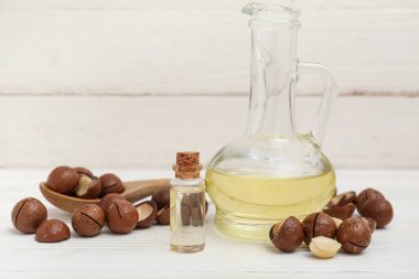 Bir sürahi macadamia yağı ve açık ahşap masada fındık.