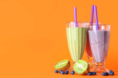 Turuncu arka planda kivi ve yaban mersinli farklı taze meyve suları.