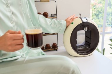 Bir fincan kahve ve modern makineli kadın mutfaktaki masada, yakın plan.