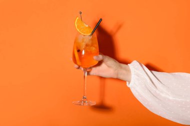 Turuncu arka planda bir bardak Aperol spreyli kadın eli.