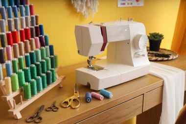 Atölyedeki terzi masasında iplik makaralı dikiş makinesi.
