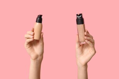 Pembe arka planda makyaj malzemesi şişeleri olan kadın elleri.