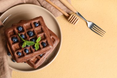 Bir tabak taze yaban mersinli Belçika waffle 'ı ve sarı arka planda nane şekeri.