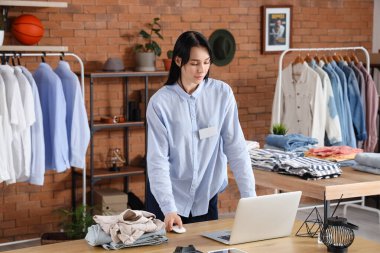 Erkek giyim mağazasındaki masada dizüstü bilgisayarla çalışan kadın satıcı.