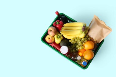 Farklı taze ürünlerle dolu yeşil alışveriş sepeti ve mavi arka planda muzlar. Üst görünüm