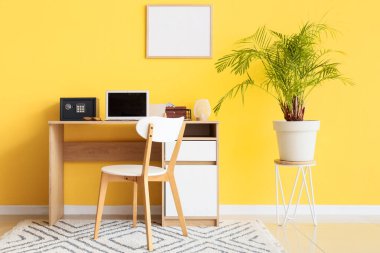 Modern bilgisayar ve kasa sarı duvarın yanındaki masada.