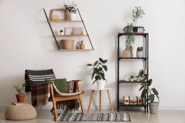 Beyaz duvarın yanında koltuğu, çiçekleri ve raf ünitesi olan modern bir oda.