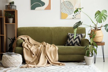 Beyaz duvarın yanında yeşil kanepesi ve raf ünitesi olan modern bir oda.