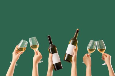 Yeşil arka planda şişeleri ve şarap kadehlerini tutan kadın eller