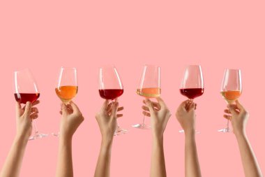 Pembe arka planda farklı şarabın kadehlerini tutan kadın eller.