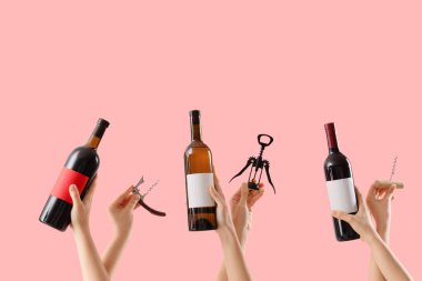 Pembe arka planda şarap şişeleri ve tirbuşon tutan kadın eller.