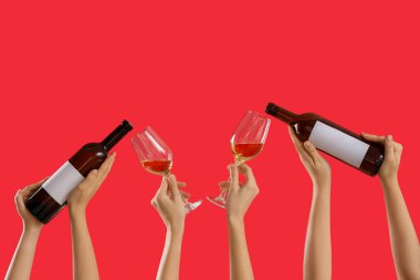 Kırmızı arka planda şarap kadehleri ve şişeleri tutan kadın eller.