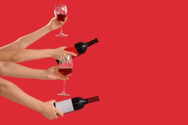 Kırmızı arka planda bardakları ve şarap şişelerini tutan kadın eller.