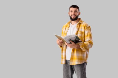 Gri arka planda dergisi olan yakışıklı, mutlu genç bir adam.