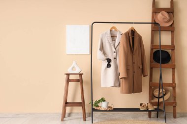 Bej duvarın yanında elbise askısı, merdiven ve sehpası olan modern tuvalet odası.