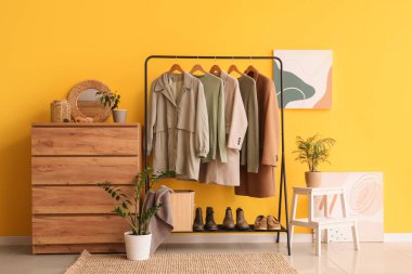 Sarı duvarın yanında elbise askısı ve şifoniyeri olan modern soyunma odasının içinde.