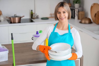 Önlüklü güzel bir kadın, mutfakta temiz tabaklar var.