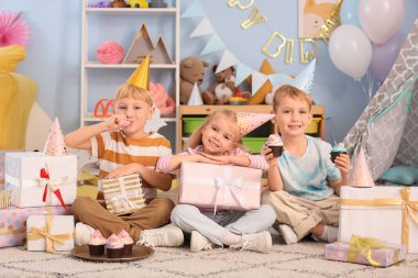 Evde doğum gününü kutlarken elinde kek ve hediye kutusuyla ıslık çalan şirin küçük mutlu çocuklar.