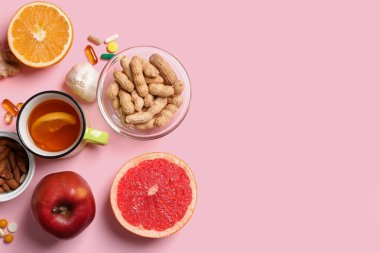 Farklı sağlıklı yiyeceklere sahip kompozisyon, bir fincan çay ve pembe arka planda haplar. Dokunulmazlık artırıcı kavram