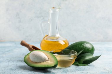 Taze avokado, kase ve sürahi yağ renkli grunge masasında.