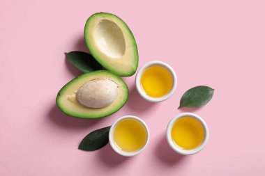 Taze avokadolu kompozisyon, pembe arka planda yağ ve bitki yaprakları.